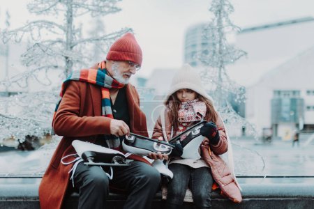 Téléchargez les photos : Grand-père avec sa petite-fille en hiver à la patinoire extérieure. Grands-parents enseignant fille mignonne comment patiner sur glace. - en image libre de droit