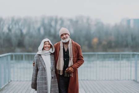Foto de Elegante pareja de ancianos caminando cerca de un río, durante el frío día de invierno. - Imagen libre de derechos