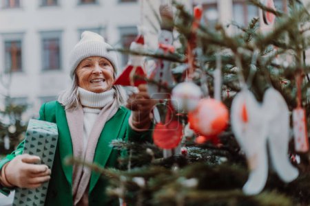 Foto de Feliz mujer mayor disfrutando del mercado de Navidad al aire libre, la compra de regalos y adornos de Navidad. - Imagen libre de derechos