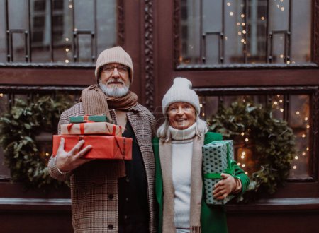 Foto de Feliz pareja de ancianos disfrutando del mercado de Navidad al aire libre en la noche, la compra de regalos y árbol de Navidad. - Imagen libre de derechos