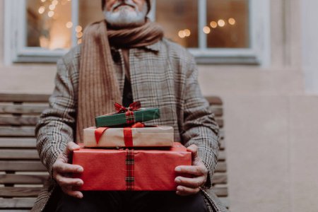 Foto de Primer plano del hombre mayor sentado en un banco, sosteniendo un montón de regalos de Navidad en sus manos. Navidad compras juerga. - Imagen libre de derechos