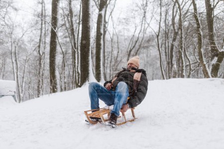 Photo for Senior man having fun during cold winter day, sledding down the hill. Elderly man spending winter vacation in the mountains. Wintry landscape. - Royalty Free Image