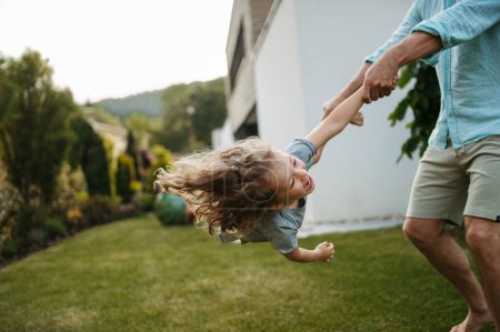 Foto de Padre sosteniendo a su hijo y girándolo en el jardín. Papá con niño divirtiéndose al aire libre. - Imagen libre de derechos