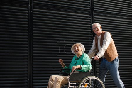 Téléchargez les photos : Portrait de couple de personnes âgées avec une femme en fauteuil roulant. Homme âgé poussant sa charmante femme en fauteuil roulant. Concept de maladie chronique chez les couples âgés. Portrait avec espace de copie sur fond noir - en image libre de droit
