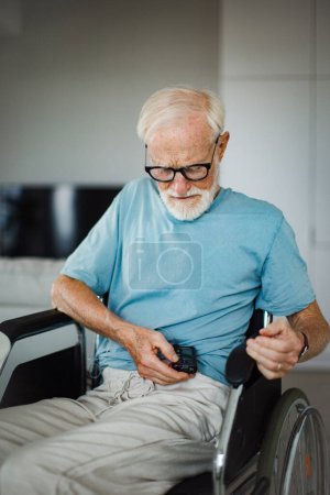 Foto de Hombre mayor comprobando su nivel de azúcar en sangre en una bomba de insulina. Primer plano del hombre mayor en silla de ruedas con diabetes tipo 1. - Imagen libre de derechos