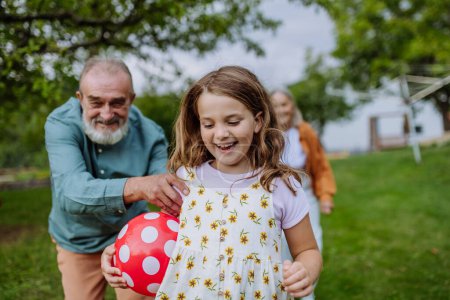 Téléchargez les photos : Les grands-parents jouent avec leurs petits-enfants dans le jardin, lançant une balle en s'amusant pendant la chaude journée d'automne. - en image libre de droit