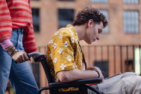 Photo for Sad gen Z boy in a wheelchair with friends in the city. Inclusion, equality, and diversity among Generation Z. Sadness and helplessness in the face of chronic illness. - Royalty Free Image