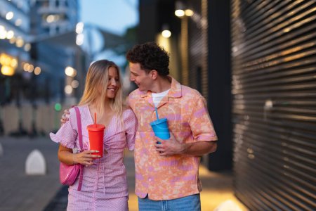 Photo for Gen Z couple in pink outfits leaving the cinema with drinks in hand. The young zoomers watched a movie addressing the topic of women, her position in the world, and body image. - Royalty Free Image