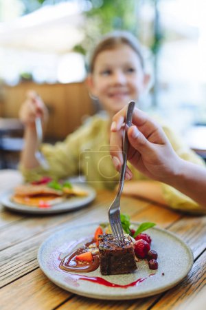 Foto de Primer plano de un plato con pastel de chocolate. Una chica comiendo panqueques en un restaurante. Cena familiar en un restaurante adecuado para familias. - Imagen libre de derechos