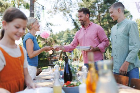 Téléchargez les photos : Table de cadre familial pour la garden party d'été. Apporter des assiettes, de la nourriture et des boissons. - en image libre de droit