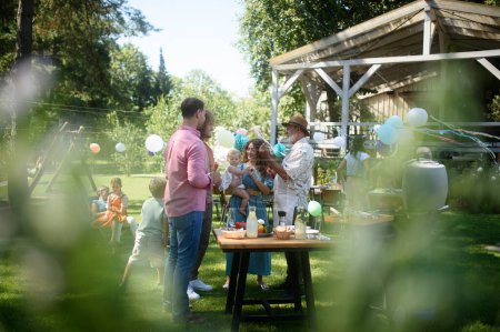 Foto de Amigos y familiares conversando y divirtiéndose en una fiesta de verano en el jardín de barbacoa, preparando comida en la parrilla. - Imagen libre de derechos