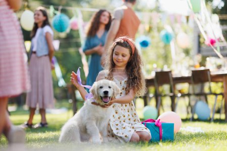 Photo for Garden birthday party for young girl. Beautiful birthday girl received a puppy as a birthday gift. - Royalty Free Image