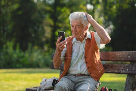 Foto de Hombre mayor sentado fuera y de compras en línea en un teléfono inteligente. El riesgo de estafas de compras en línea dirigidas a las personas mayores. - Imagen libre de derechos