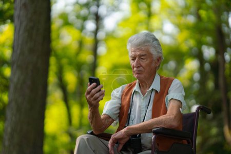 Foto de Hombre mayor en silla de ruedas de compras en línea en un teléfono inteligente. El riesgo de estafas de compras en línea dirigidas a las personas mayores. - Imagen libre de derechos