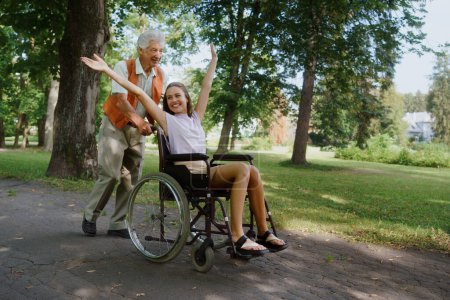 Photo for The senior man pushing young caregiver in a wheelchair, having fun. The elderly man feeling good and fit, he is able to push his granddaughter in the wheelchair. - Royalty Free Image