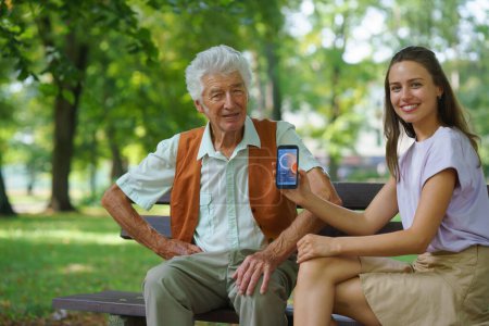 Téléchargez les photos : Aide soignant homme diabétique aîné vérifier ses données de glucose sur smartphone. Aîné diabétique utilisant un glucomètre continu. Petite-fille enseignant à son grand-père à utiliser un smartphone, tapant des textes - en image libre de droit