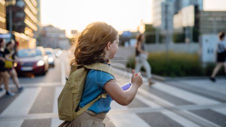 Téléchargez les photos : Vue latérale d'une fille avec un sac à dos traversant le passage pour piétons sur le chemin de l'école. Concept de retour à l'école. - en image libre de droit