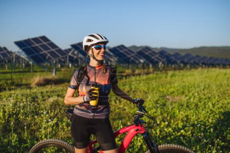 Foto de Retrato de un hermoso ciclista de pie frente a paneles solares en una granja solar, agua potable. Una granja solar como solución para un futuro energético más sostenible. - Imagen libre de derechos