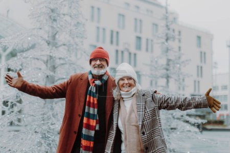 Foto de Elegante pareja de ancianos en la ciudad de Navidad durante el frío día de invierno. Mayores que se tambalean con los brazos abiertos. - Imagen libre de derechos