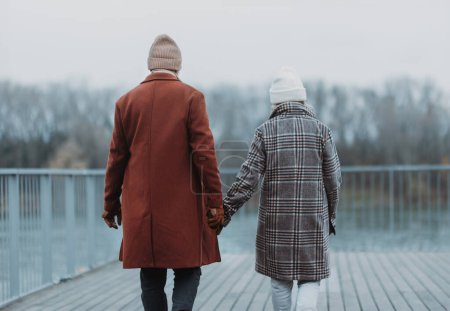 Photo for Rear view of elegant senior couple walking near a river, during cold winter day. - Royalty Free Image