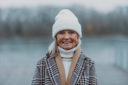 Téléchargez les photos : Femme âgée élégante marchant près d'une rivière, pendant la journée froide d'hiver. Bannière d'hiver avec espace de copie. - en image libre de droit