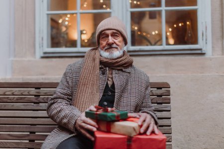 Foto de Primer plano del hombre mayor sentado en un banco, sosteniendo un montón de regalos de Navidad en sus manos. Navidad compras juerga. - Imagen libre de derechos