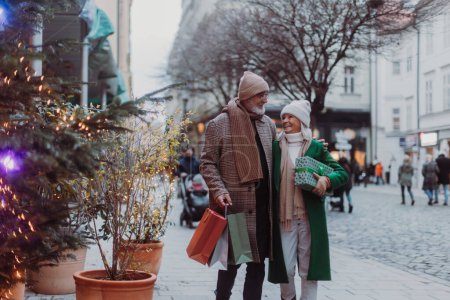 Glückliches Senioren-Paar kauft Weihnachtsgeschenke in den winterlichen Straßen der Stadt.