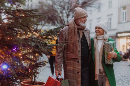 Téléchargez les photos : Heureux couple de personnes âgées achetant des cadeaux de Noël dans les rues de la ville d'hiver. - en image libre de droit