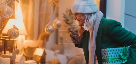 Foto de Elegante anciana está mirando a una pantalla de la ventana. La señora mayor está comprando regalos de Navidad en la ciudad. Banner con espacio de copia. - Imagen libre de derechos