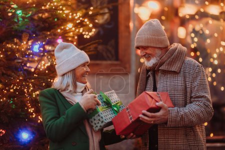 Téléchargez les photos : Heureux couple de personnes âgées profitant du marché de Noël en plein air le soir, l'achat de cadeaux et d'arbre de Noël. - en image libre de droit