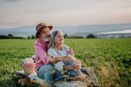 Téléchargez les photos : Embrasser couple de personnes âgées regarder coucher de soleil à la nature d'automne, pique-niquer. - en image libre de droit