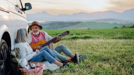 Potrait des Ehemanns, der Gitarre spielt und seiner Frau ein Ständchen bringt. Ältere Eheleute bei einem herbstlichen Roadtrip und beobachten den Sonnenuntergang hinter der Hohen Tatra. Herbstbanner mit Kopierraum.