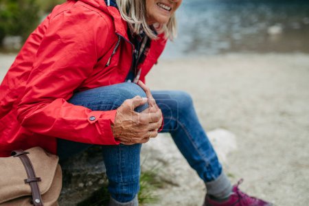 Photo for Senior woman injured leg during hike in the mountains. Tourist went off-trail and fell. Elderly tourist feeling pain under kneecap, also known as Hikers knee. - Royalty Free Image