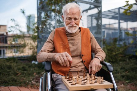 Téléchargez les photos : Un aîné jouant aux échecs seul dehors. Soins infirmiers client de la maison, profiter d'un jeu d'échecs solitaire, puzzle d'échecs. - en image libre de droit