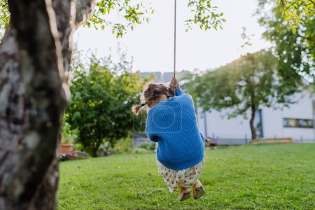Téléchargez les photos : Une jeune fille balançant sur une balançoire dans le jardin. L "écolière passe du temps libre avec ses grands-parents dans le jardin par une chaude journée d'automne. - en image libre de droit