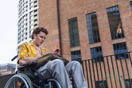 Photo for Gen Z boy in a wheelchair in the city using smartphone. Inclusion, equality, and diversity among Generation Z. - Royalty Free Image