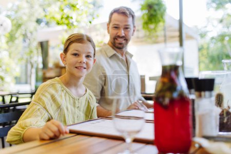 Téléchargez les photos : Père et fille lisant des menus dans un restaurant, choisissant de la nourriture et des boissons. Dîner en famille dans un restaurant. - en image libre de droit