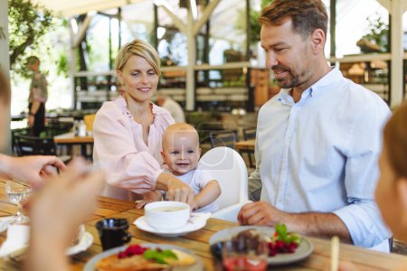 Téléchargez les photos : Famille avec bébé en chaise haute manger de la nourriture au restaurant. Dîner en famille dans un restaurant. - en image libre de droit