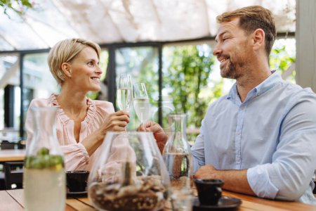 Photo for Portrait of beautiful couple in a restaurant, on a romantic date. Husband and wife are clinking champagne glasses, making a toast at restaurant patio. - Royalty Free Image