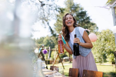 Photo for Young beautiful woman preparing drinks for a summer garden party. The hostess is holding bottles of wine. - Royalty Free Image