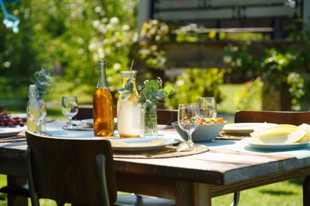Gros plan d'une table dressée lors d'une garden party estivale. Table avec verres, limonade, fruits frais et salade et décoration florale délicate.