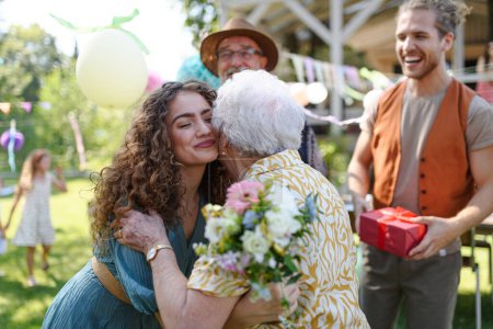 Foto de Fiesta de cumpleaños en el jardín para la señora mayor. Hermosa mujer de cumpleaños mayor abrazando a su nieta. - Imagen libre de derechos