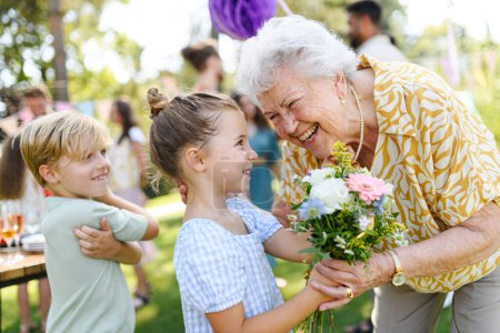 Foto de Fiesta de cumpleaños en el jardín para la señora mayor. Hermosa mujer de cumpleaños mayor que recibe flores de nieta y nieto. - Imagen libre de derechos