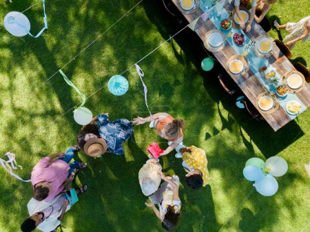 Photo for Top view of a garden party with decorations and a set table. The birthday girl greeting guests and receiving birthday wishes and gifts. - Royalty Free Image