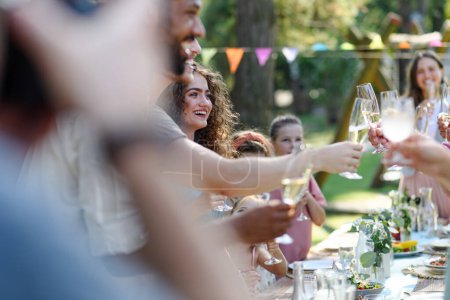 Photo for Group of friends clinking glasses at garden party. Celebratory toast at the party table. - Royalty Free Image