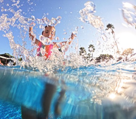Photo for Little girl splashing water in the pool, playing in the water and having fun. Beach resort vacation by the sea. Winter or summer seaside holiday. - Royalty Free Image