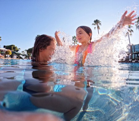 Téléchargez les photos : Mère enseignant à sa fille à nager dans la piscine pendant les vacances d'été. Mère et fille jouant dans l'eau. Vacances balnéaires au bord de la mer. Vacances d'hiver ou d'été au bord de la mer. Sous-jacent - en image libre de droit