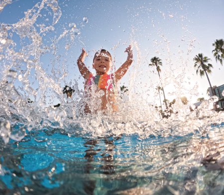 Téléchargez les photos : Petite fille éclaboussant l'eau dans la piscine, jouant dans l'eau et s'amusant. Vacances balnéaires au bord de la mer. Vacances d'hiver ou d'été à la mer. - en image libre de droit