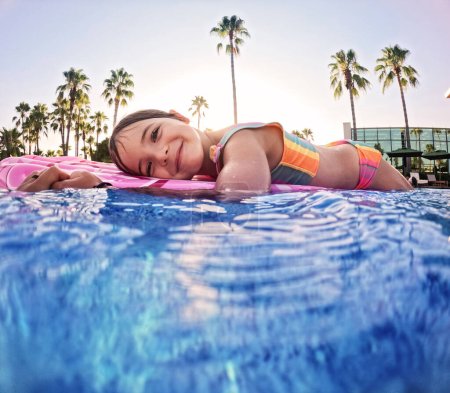 Téléchargez les photos : Adorable fille flotte sur un rose gonflable dans la piscine. Vacances balnéaires au bord de la mer. Vacances d'hiver et d'été en station balnéaire. Photographie sous-marine. - en image libre de droit