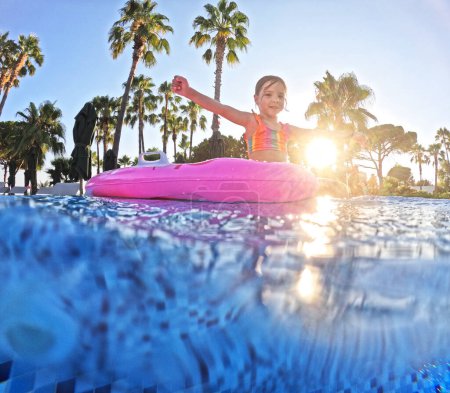 Téléchargez les photos : Adorable fille flotte sur un rose gonflable dans la piscine. Vacances balnéaires au bord de la mer. Vacances d'hiver et d'été en station balnéaire. Photographie sous-marine. - en image libre de droit